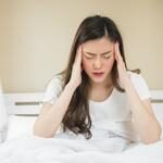 women having headache in her forehead and head sitting on bed after wake up